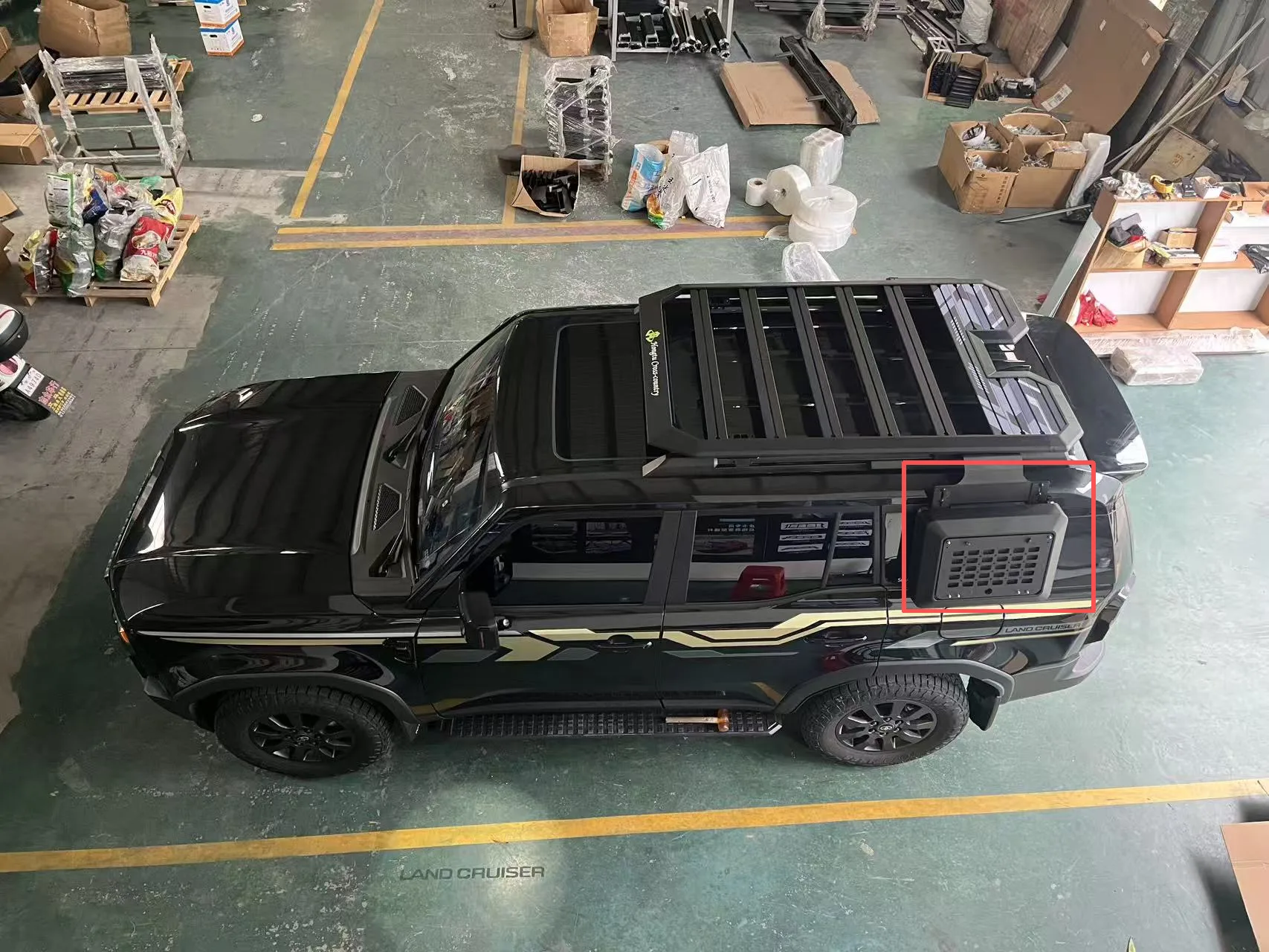 Black and silver storage box mounted beside a roof rack on an unidentified black vehicle