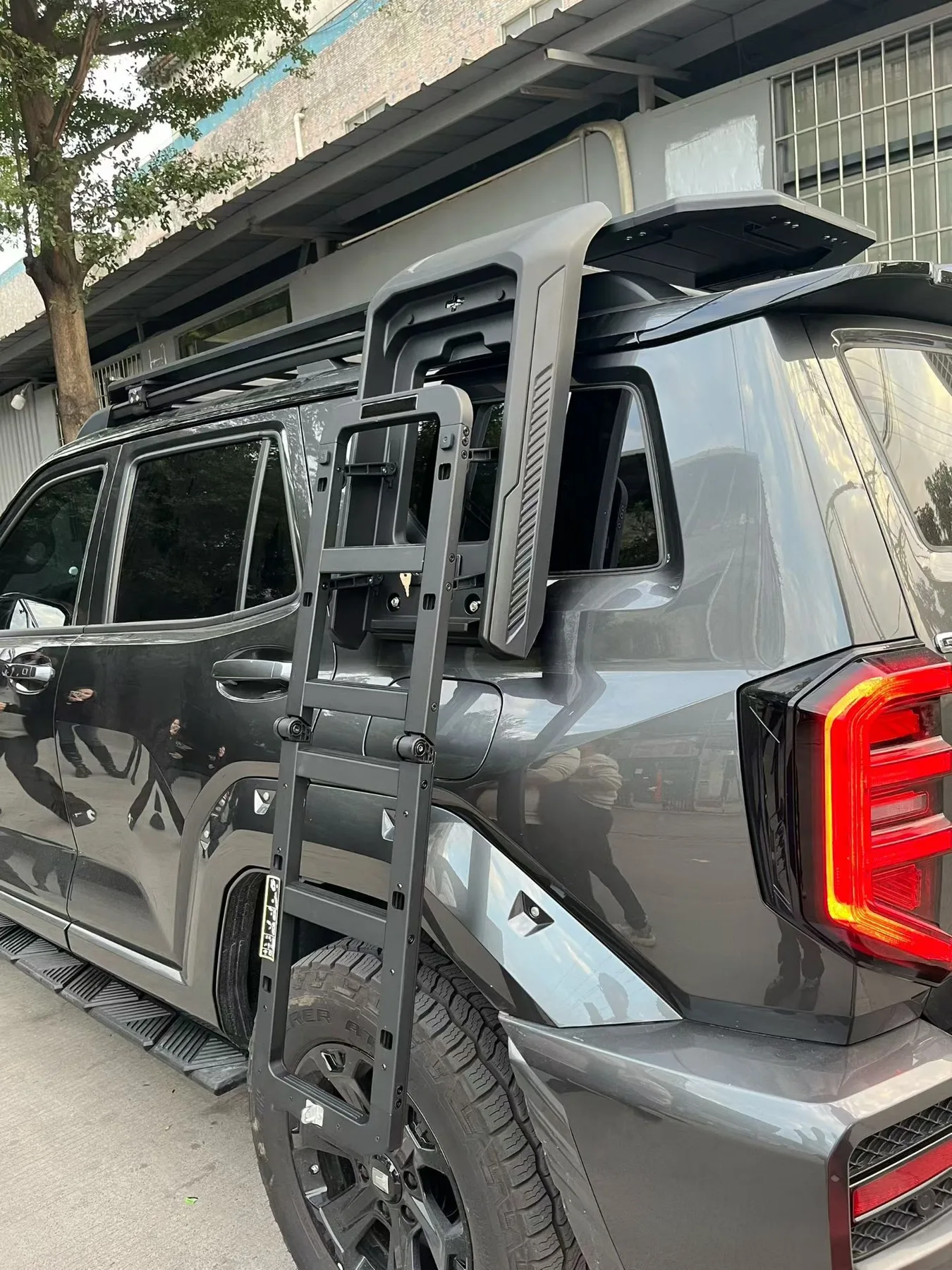 Black folding ladder mounted beside the rear of an unidentified gray vehicle