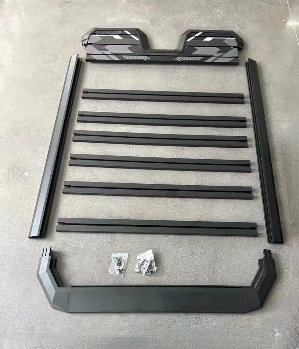 Disassembled black roof rack frame, crossbars, fairings, and hardware laid out on the floor